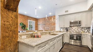 A modern kitchen with white cabinets, a granite countertop, a stainless steel oven, and a microwave.
