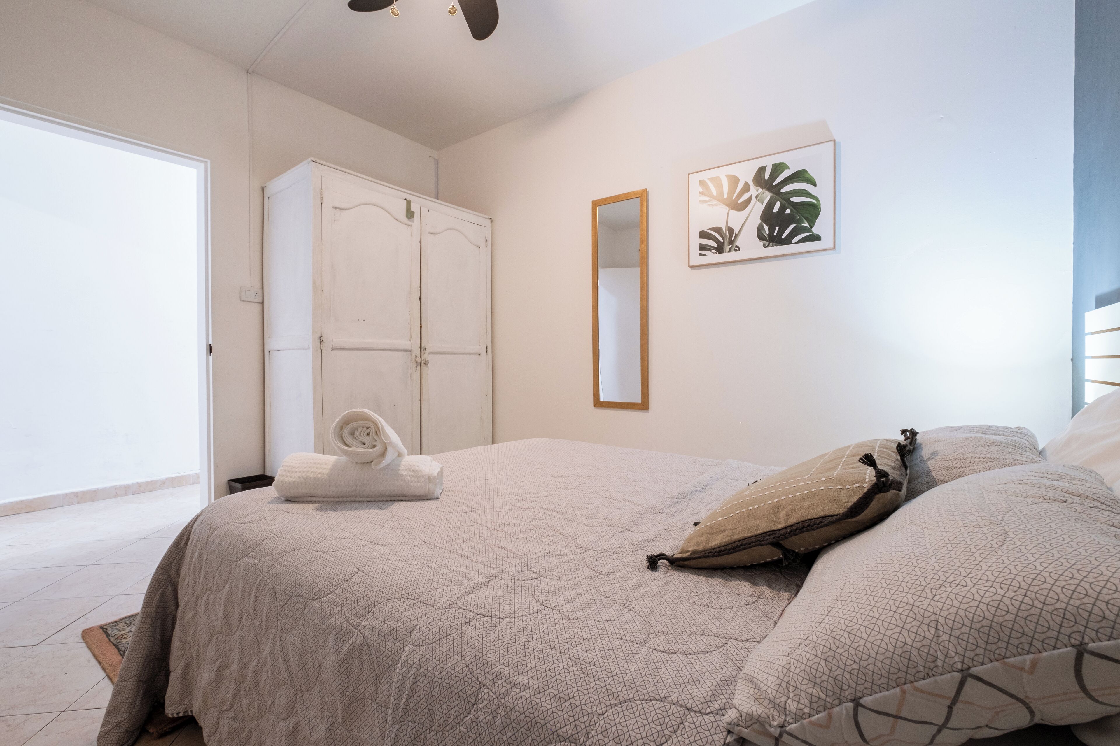 Un dormitorio con cama, armario, espejo y una obra enmarcada en la pared.