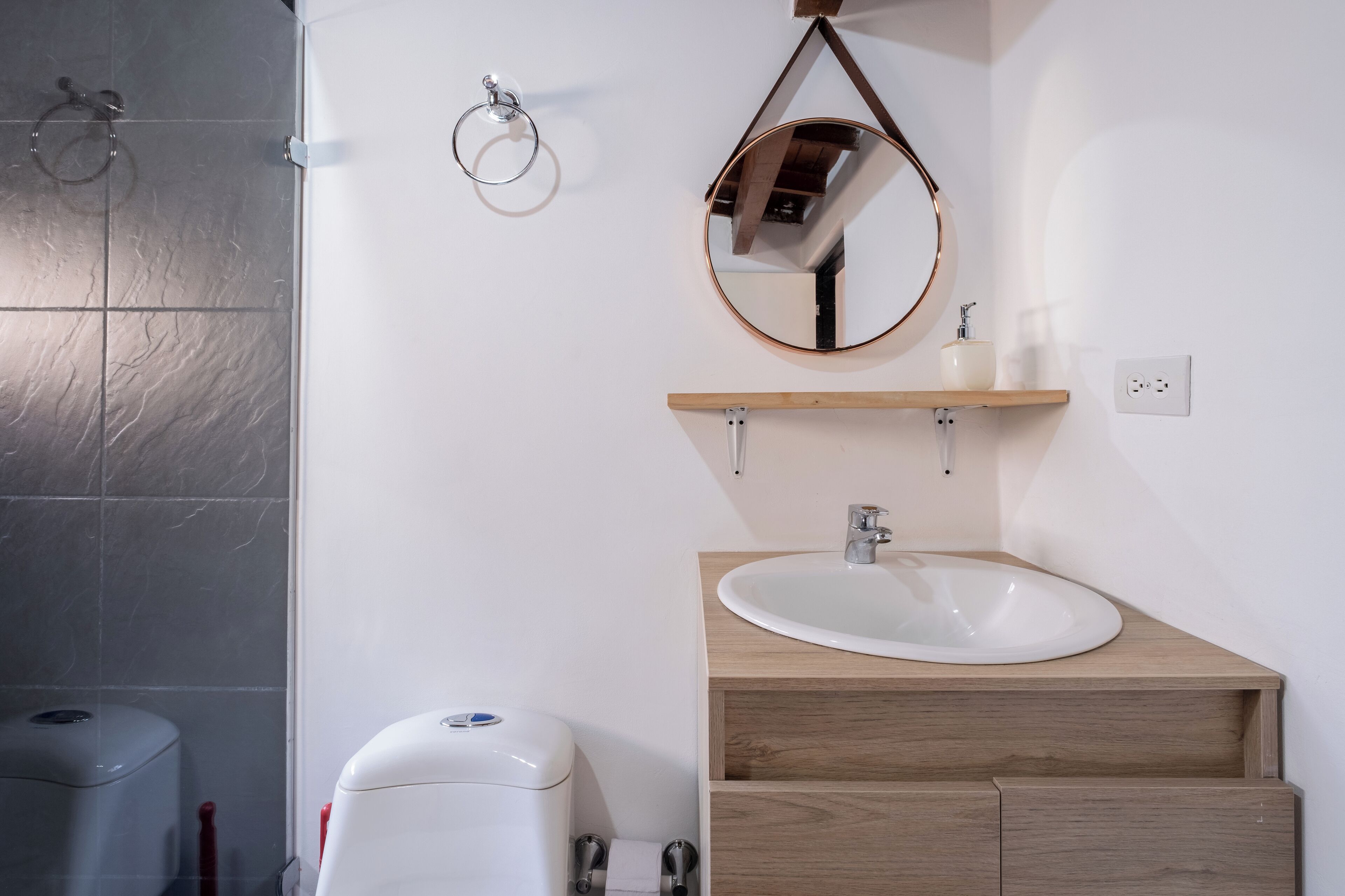 Une salle de bain avec un lavabo blanc, un meuble-lavabo en bois et un miroir rond.