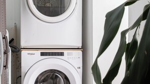 Una lavadora y secadora apiladas en un cuarto de lavado con piso de azulejos y una planta en maceta.