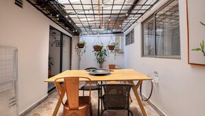 Un comedor con una mesa de madera, dos sillas, plantas colgantes y piso de baldosas.
