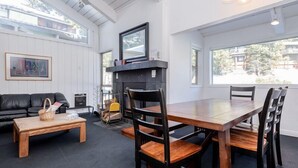 Una sala de estar moderna con una mesa de comedor de madera, sillas negras, un sofá negro y una chimenea.