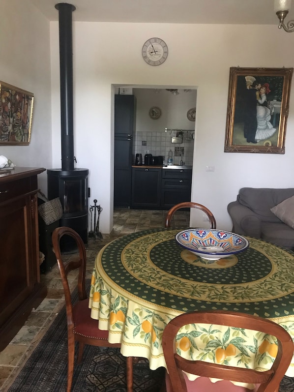 A dining area with a round table, chairs, a stove, and a kitchen in the background.