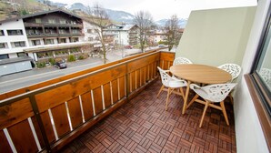 Een balkon met een houten hekwerk, een geplaveid terras en een tafel met witte stoelen.