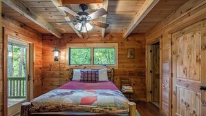 Un dormitorio de cabaña de madera con una cama, un ventilador de techo, una ventana y una puerta.