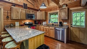 Cocina de cabaña de madera con encimeras de granito, estufa de acero inoxidable, microondas y lavavajillas.