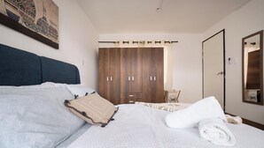 Une chambre à coucher avec un lit, des oreillers, une serviette enroulée, une armoire et un miroir.