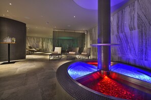 A spa area with a heated stone bath, seating area, and marble walls. - Grand Hotel Hradec (Pec pod Snezkou)