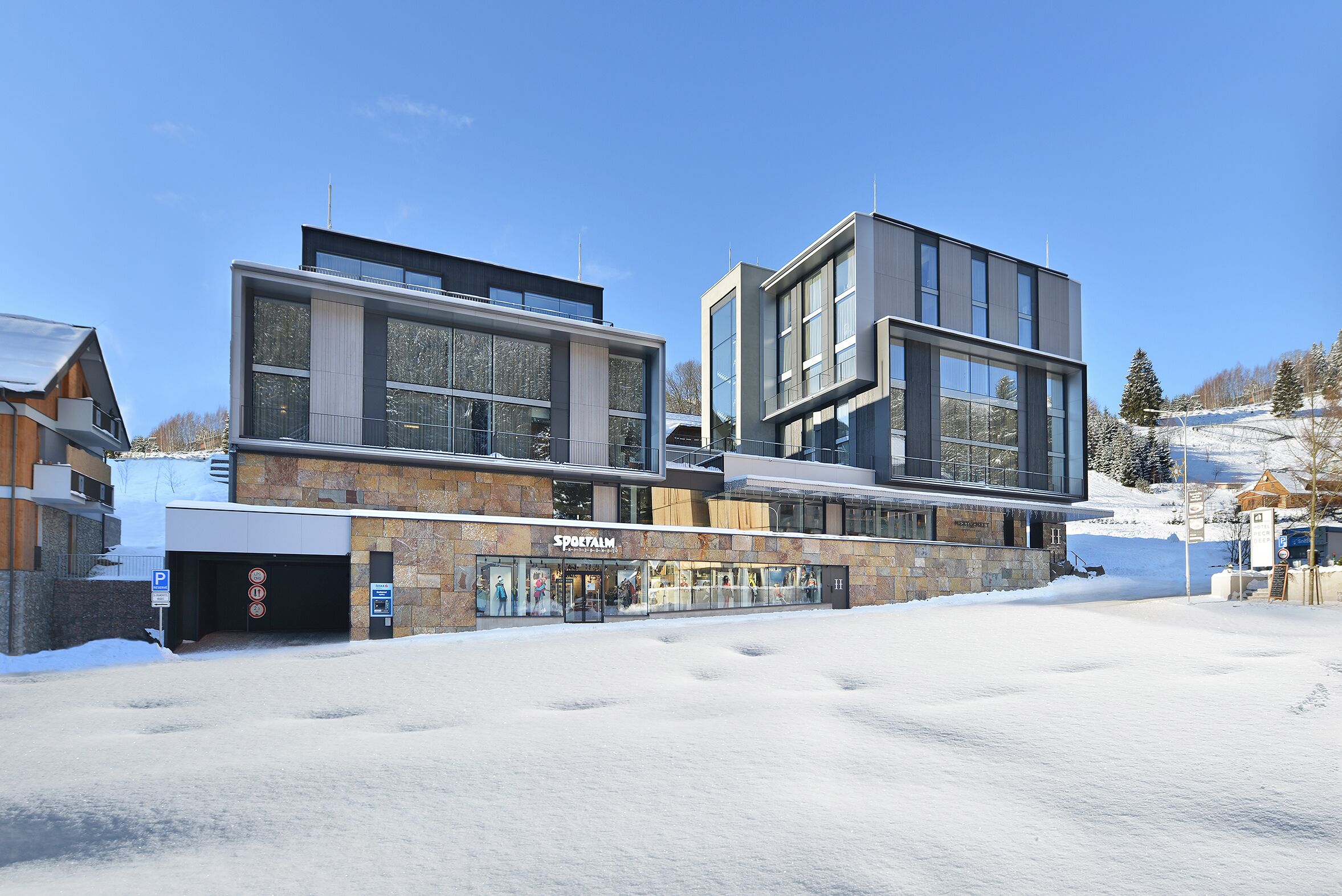 A modern building with large windows and a stone facade, featuring a shop named "Sportalm" on the ground floor.