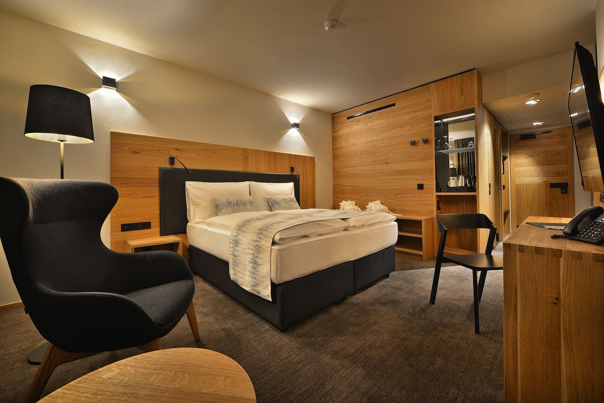 Ein modernes Hotelzimmer mit einem großen Bett, einem Schreibtisch, einem Stuhl und einem Kleiderschrank.