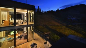 A modern hotel with a glass exterior, a balcony with seating, and a view of the surrounding landscape. - Grand Hotel Hradec (Pec pod Snezkou)