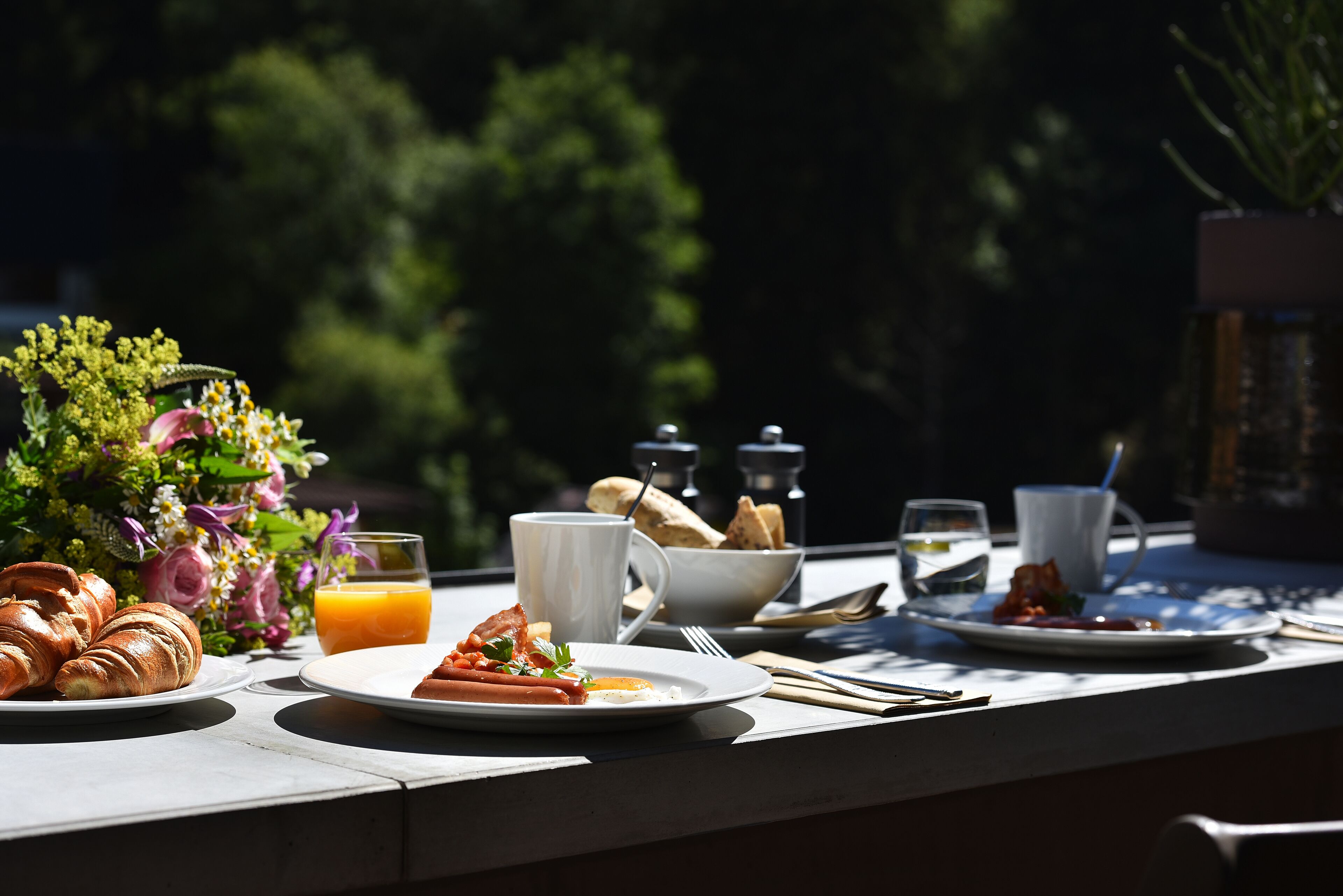 A breakfast table with croissants, a plate of food, a glass of orange juice, and a bouquet of flowers.