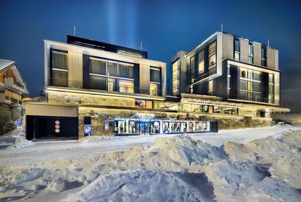 A modern hotel with a glass facade, a ground-level restaurant, and a snow-covered parking area. - Grand Hotel Hradec (Pec pod Snezkou)