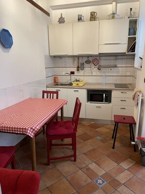 A compact kitchen with white cabinets, a red checkered table, and a red chair.