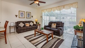 A living room with two sofas, a coffee table, a TV, and a ceiling fan. - Windsor_palms_2323n (Kissimmee)