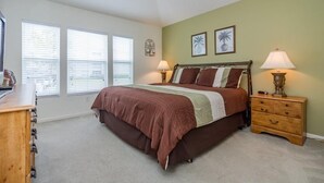 A bedroom with a large bed, two bedside lamps, a wooden nightstand, and a ceiling fan. - Windsor_palms_2323n (Kissimmee)