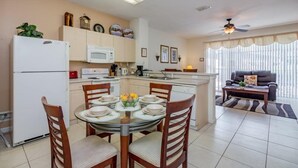 A compact kitchen with a refrigerator, microwave, and dining area with a round table and chairs. - Windsor_palms_2323n (Kissimmee)