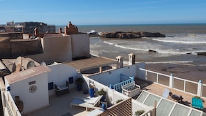 Une terrasse sur le toit offrant une vue sur la mer, des murs blancs et quelques plantes en pot.