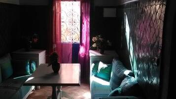 A room with a dining table, two sofas, a window with curtains, and a wall with a decorative pattern.