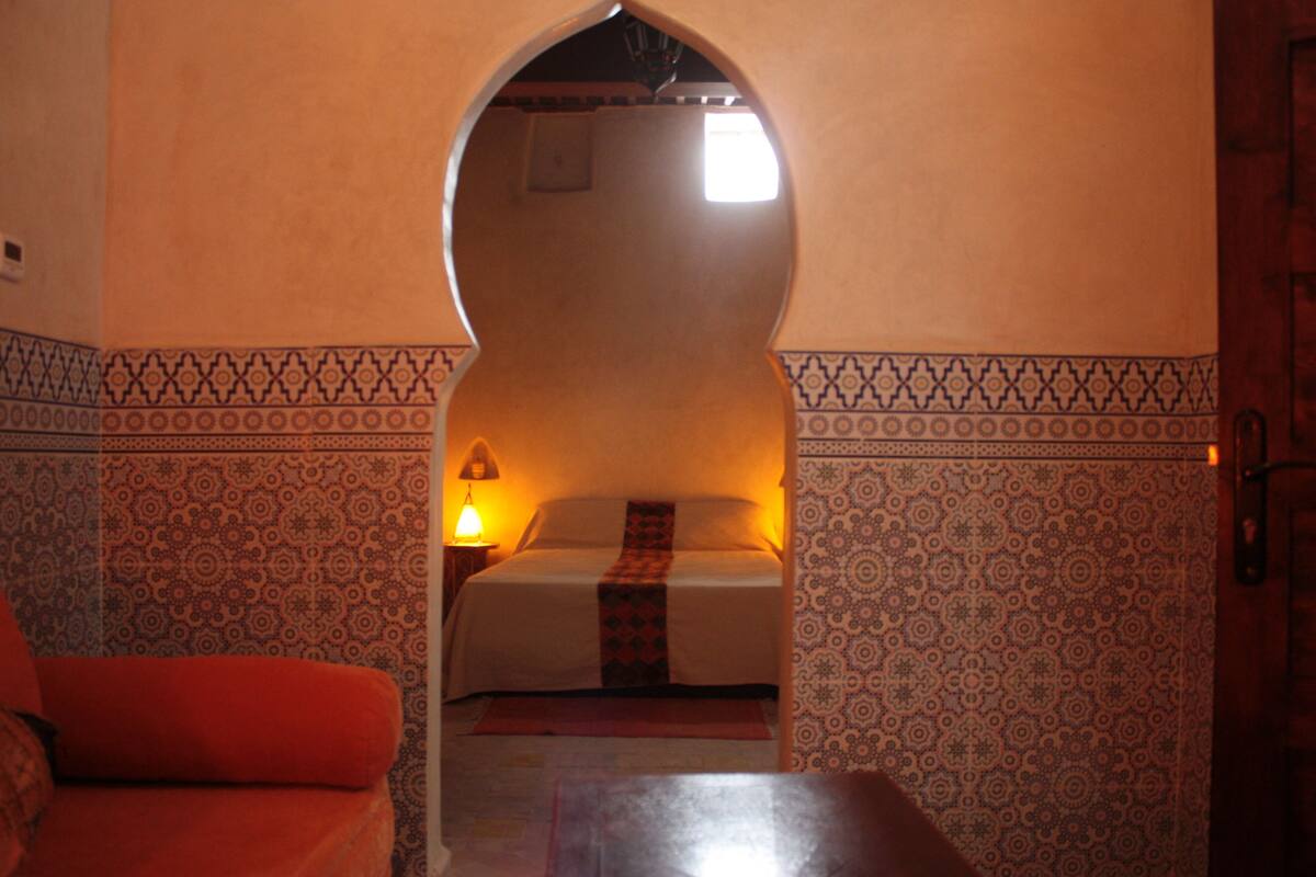 Une pièce avec un lit, une chaise rouge et une table.