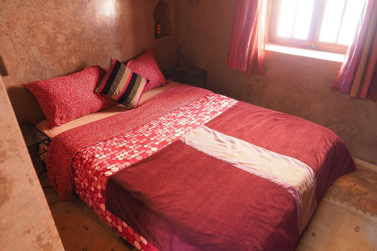 Un lit avec une literie rouge et un couvre-lit à motifs.
