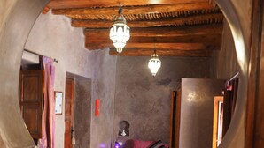 Un couloir étroit doté d’un plafond en bois et d’un lustre, qui mène à une pièce contenant un lit et un canapé violet.
