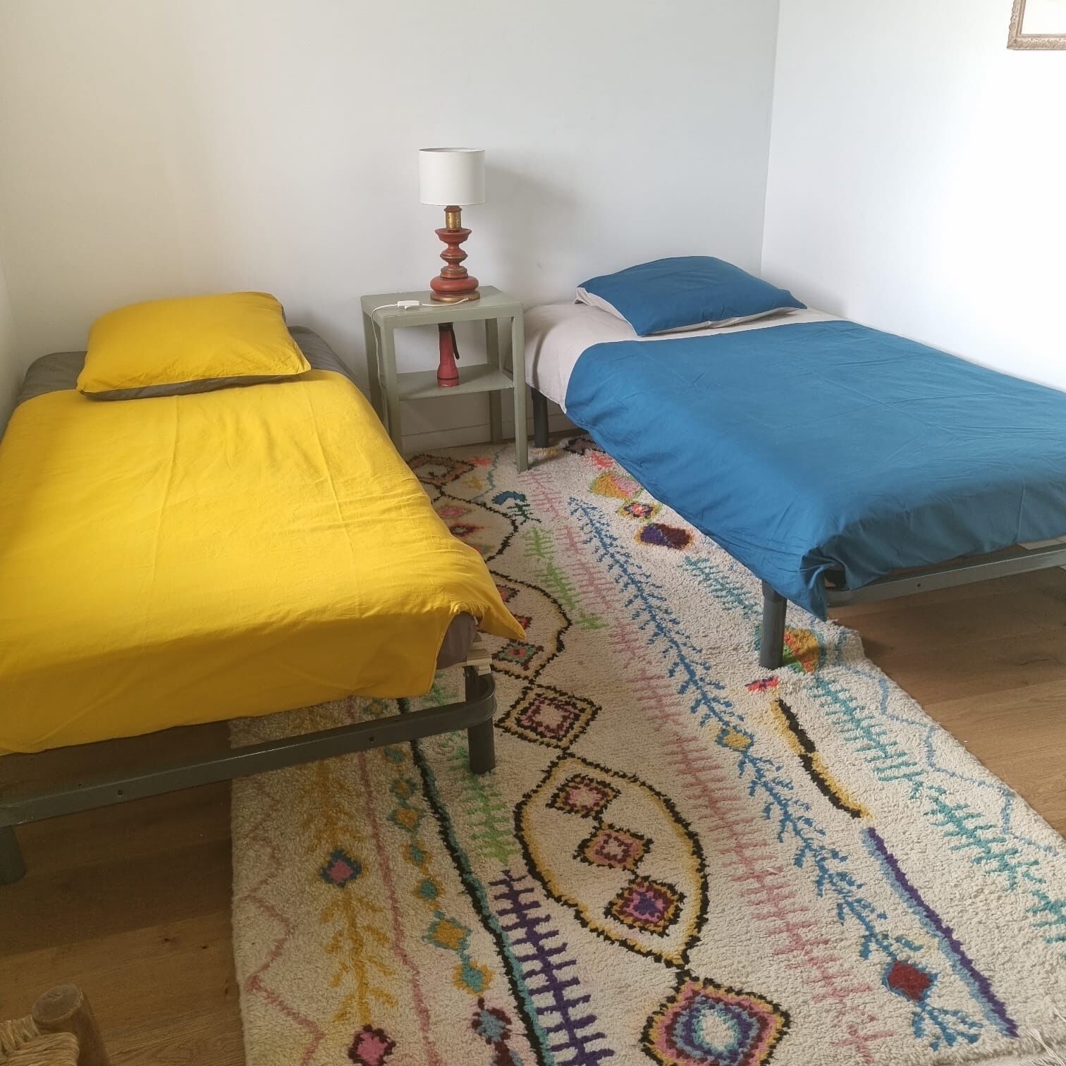 A room with two beds, a patterned rug, and a nightstand with a lamp.