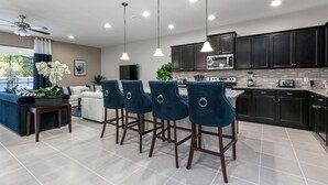 Una cocina moderna con armarios oscuros, una isla central, taburetes de bar e iluminación colgante.