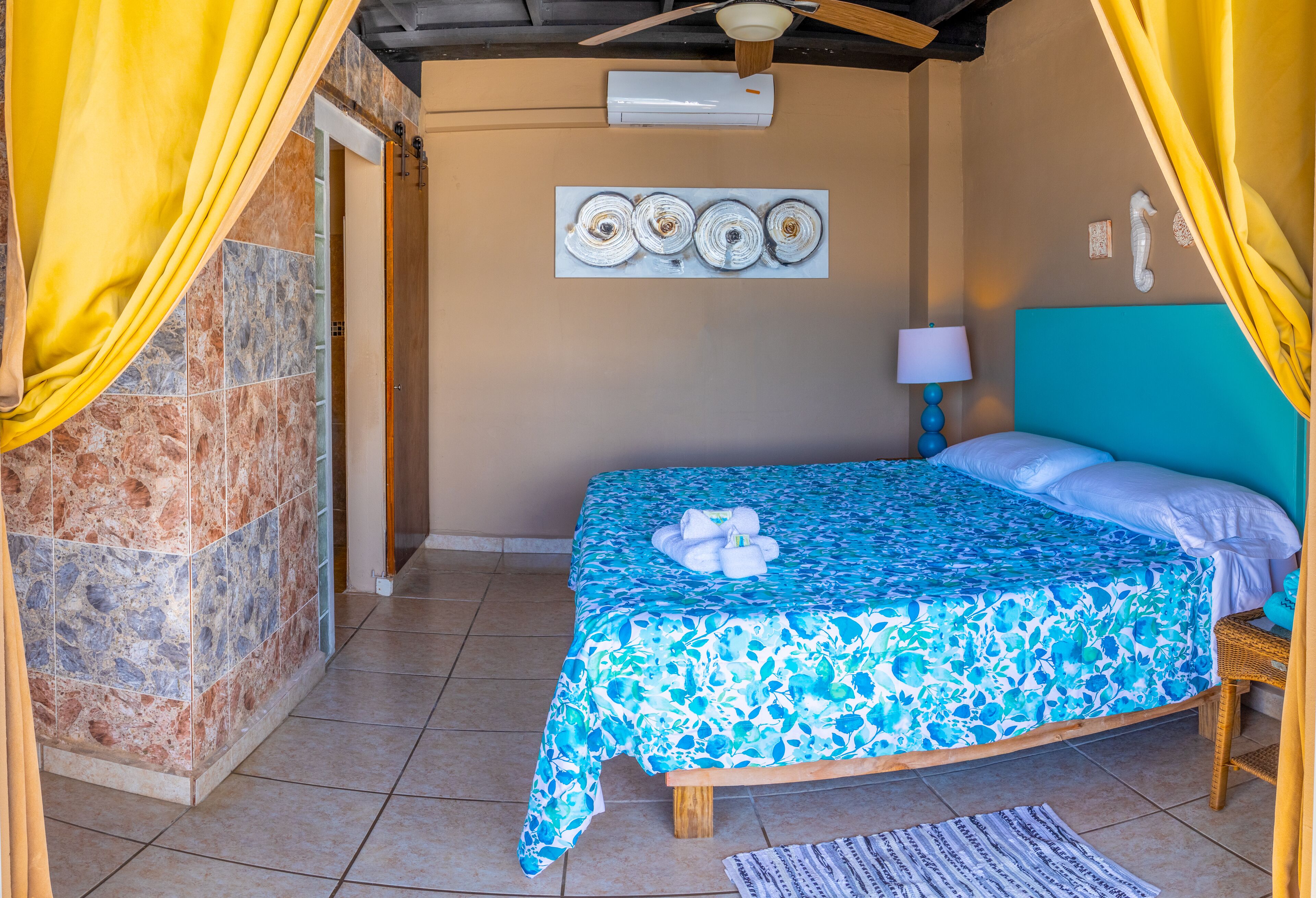 Una habitación con una cama, aire acondicionado instalado en la pared, un cuadro y una lámpara.