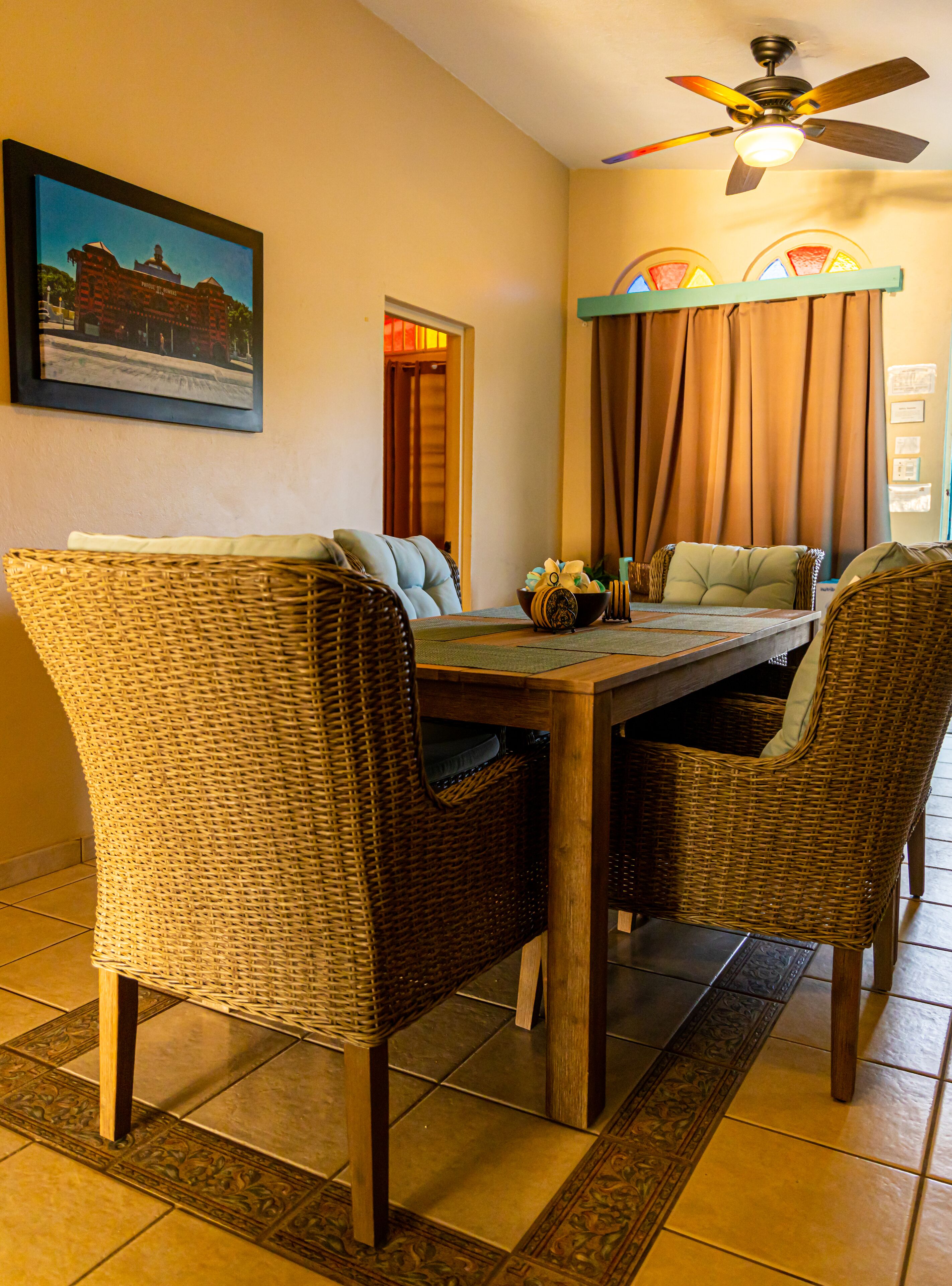 A dining area with wicker chairs, a wooden table, and a ceiling fan.