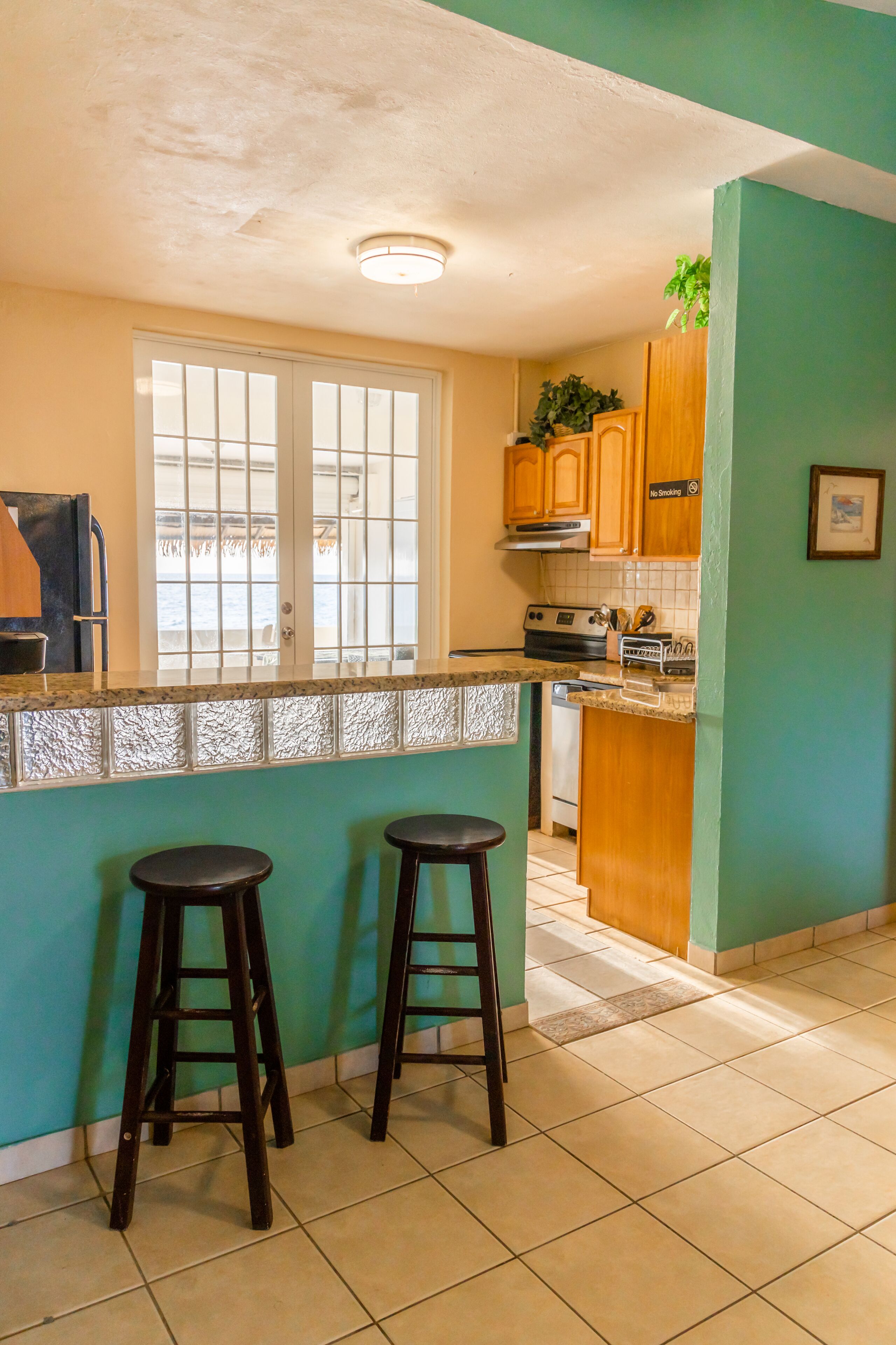 A kitchen with a window, wooden cabinets, and two stools.