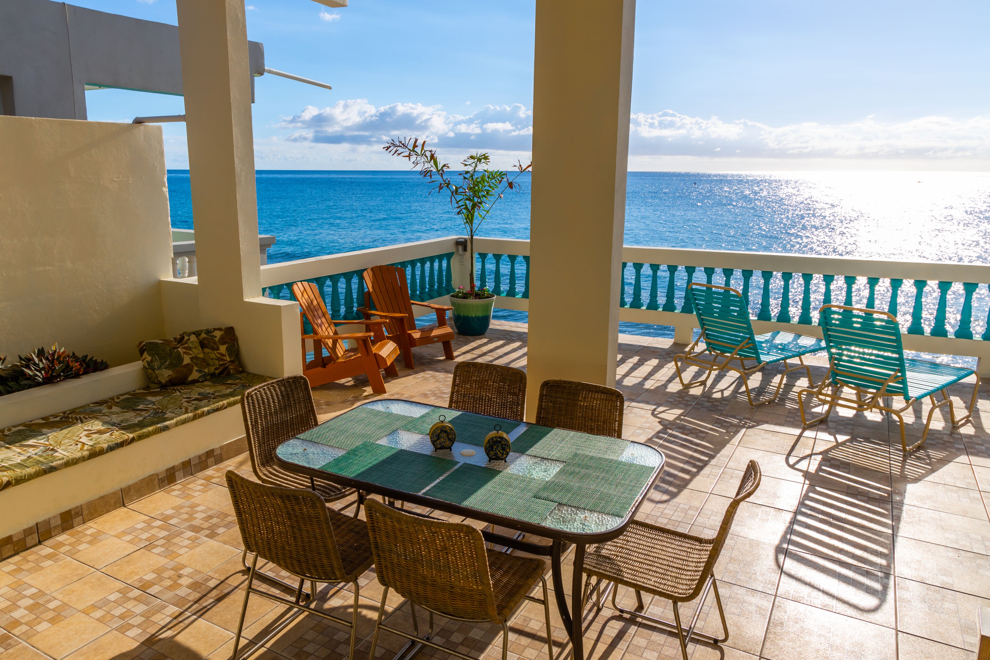 A terrace with a table and chairs, a potted plant, and a view of the ocean.