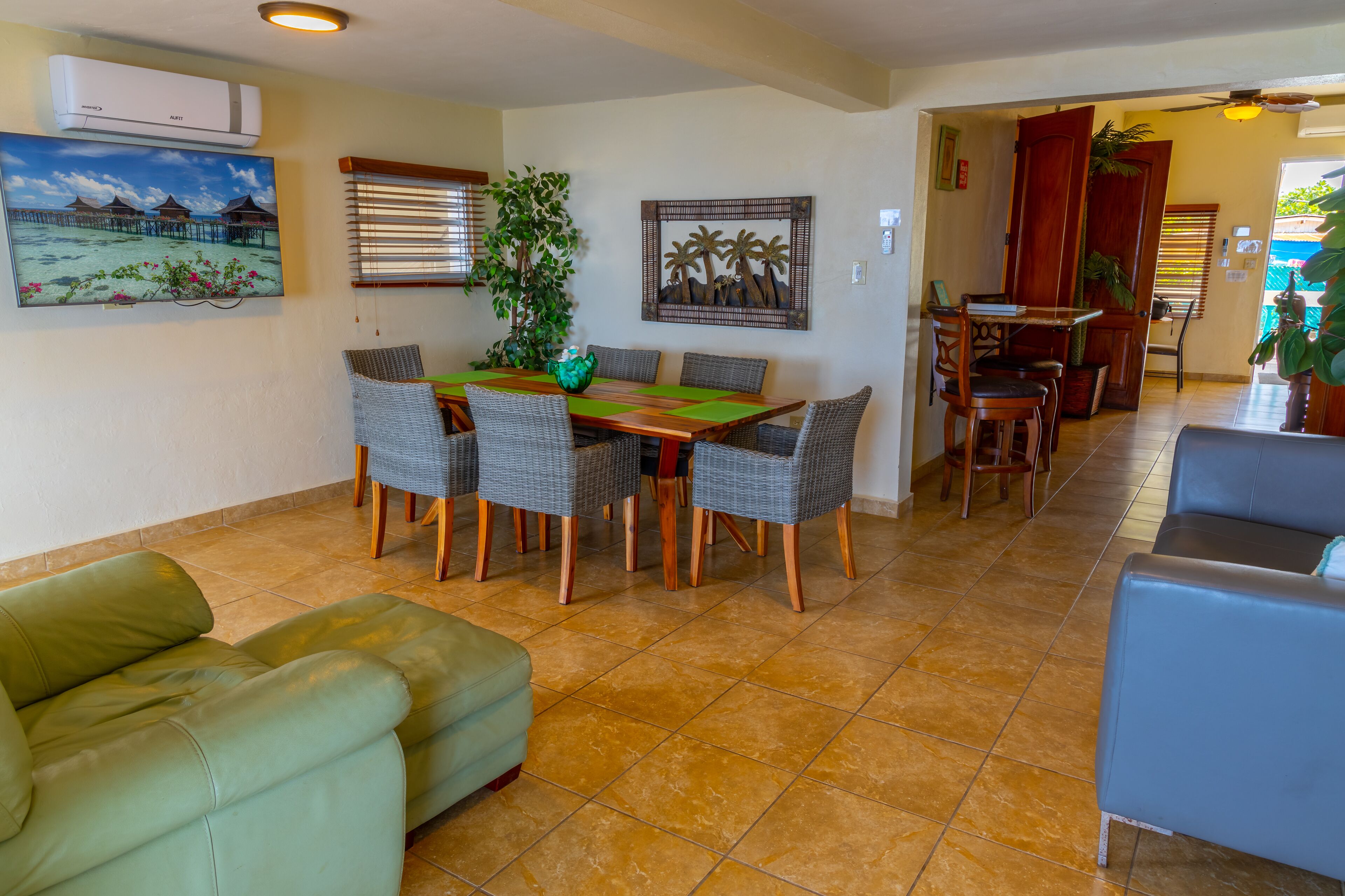 A dining area with a wooden table and wicker chairs, a green sofa, and a blue armchair.
