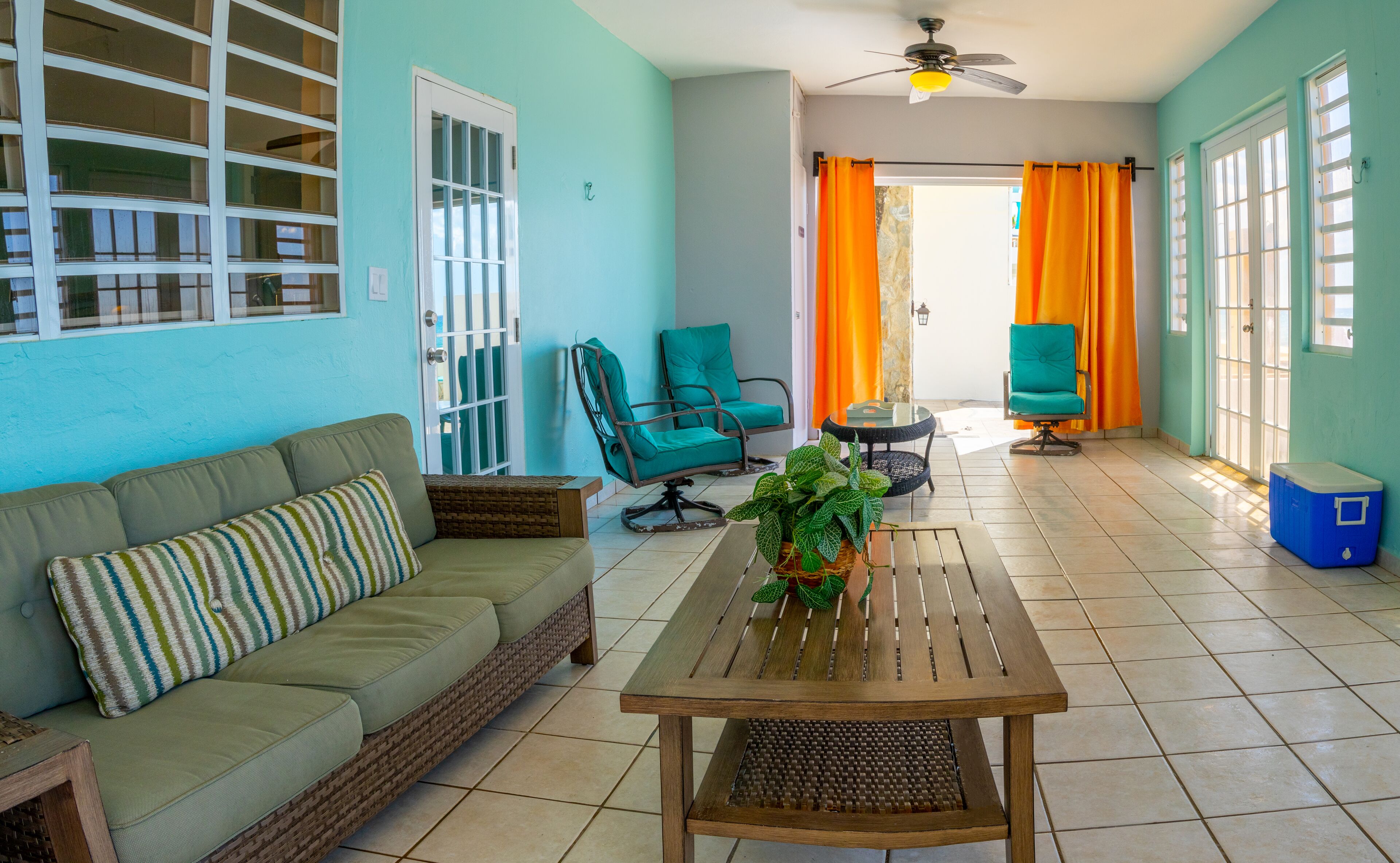 A room with a green sofa, two teal chairs, a wooden table, and a ceiling fan.