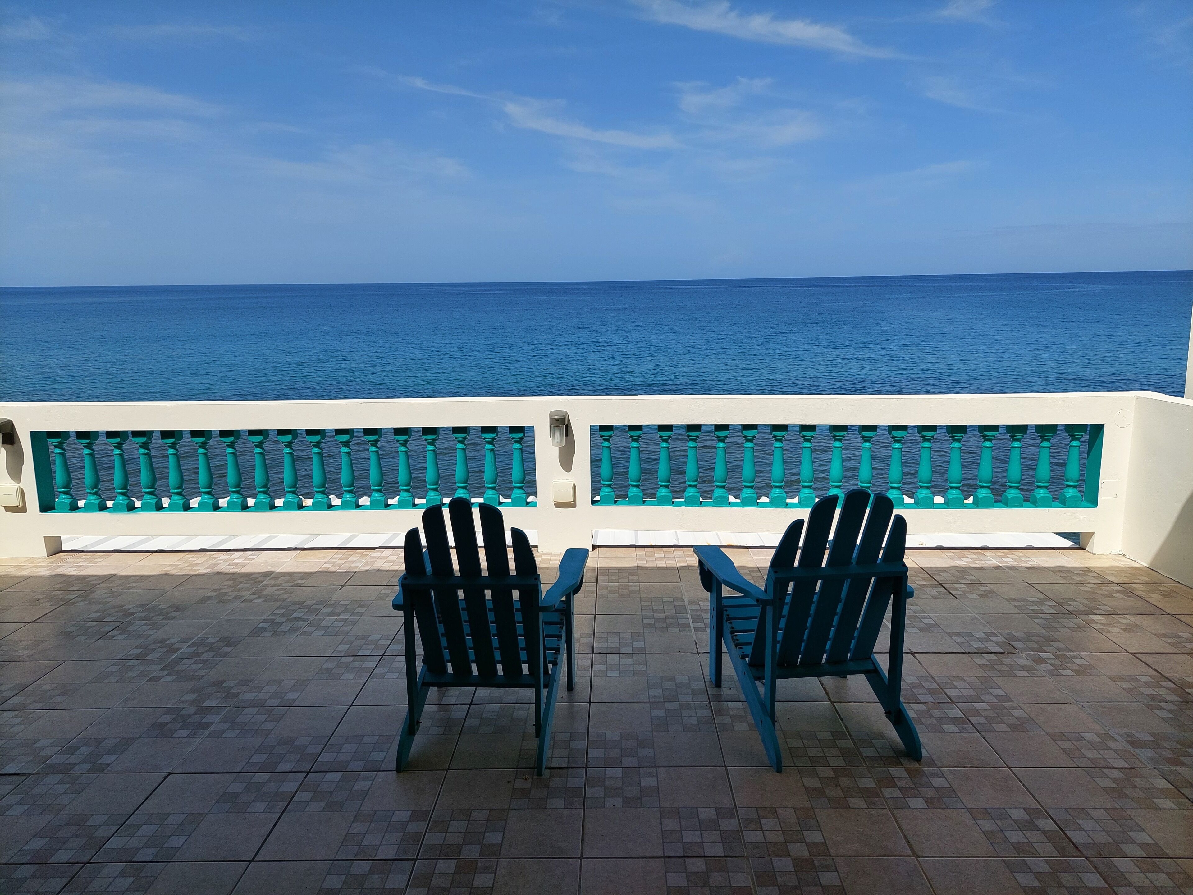 A terrace with two chairs facing a railing overlooking the sea.