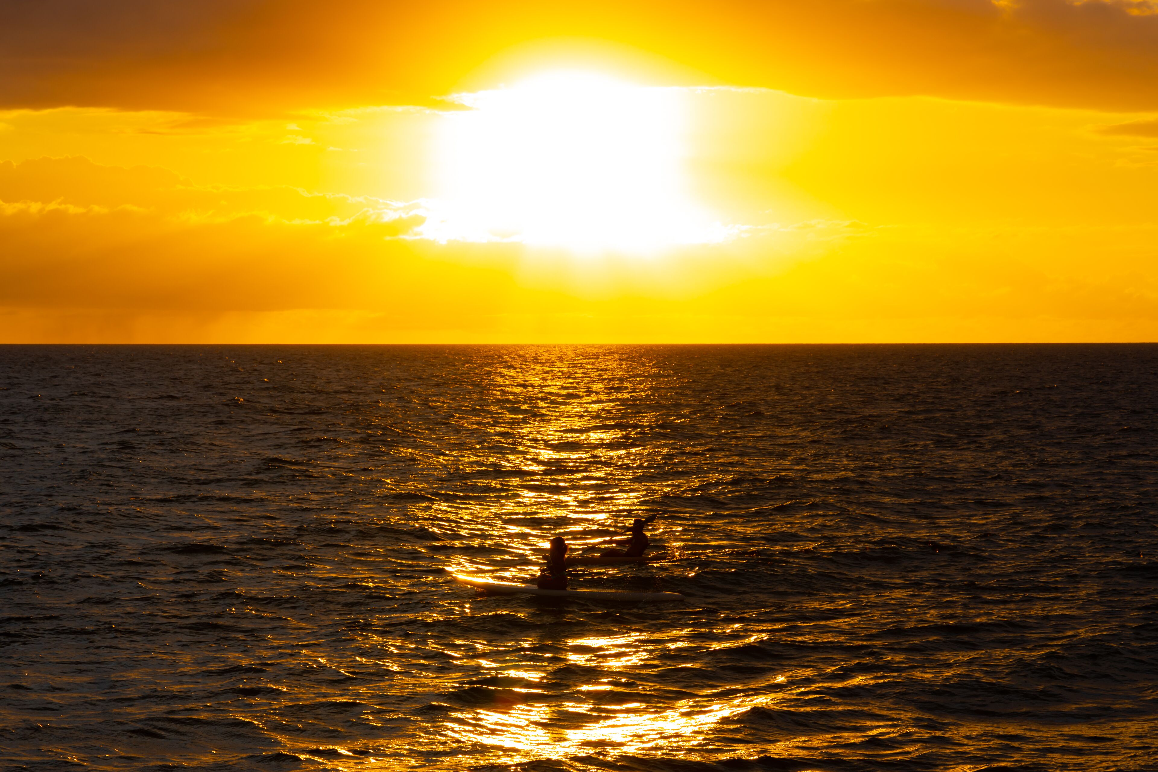 Atardecer sobre el océano con dos personas nadando.