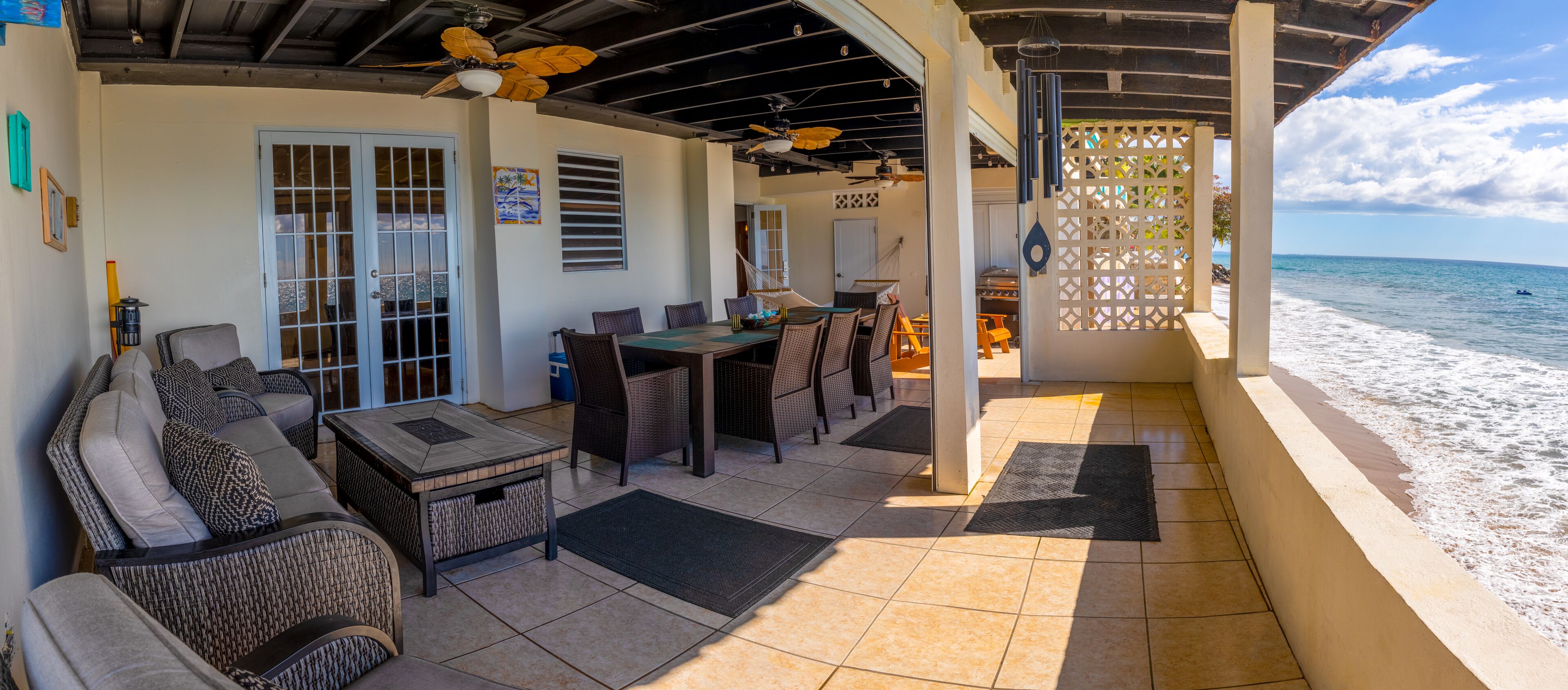 A covered outdoor seating area with wicker furniture, a table, and a view of the beach.