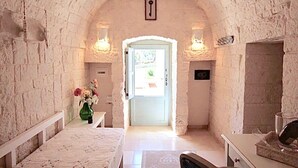 Un pasillo de paredes de piedra con una puerta blanca, un banco y un jarrón de flores.