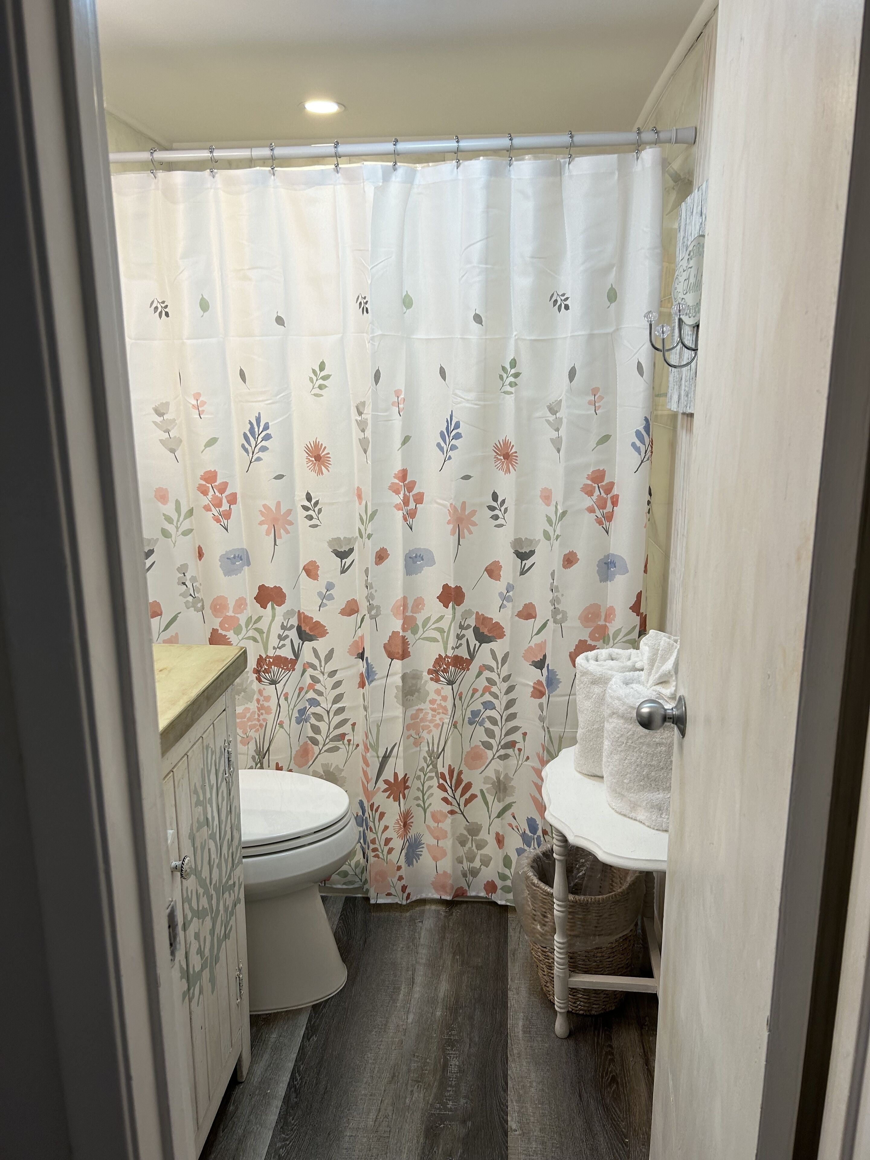 Une petite salle de bain comprenant des toilettes, un lavabo et un rideau de douche orné d’un motif floral.