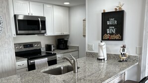 Una cocina moderna con armarios blancos, encimera de granito, electrodomésticos de acero inoxidable y una zona de bar con taburetes.