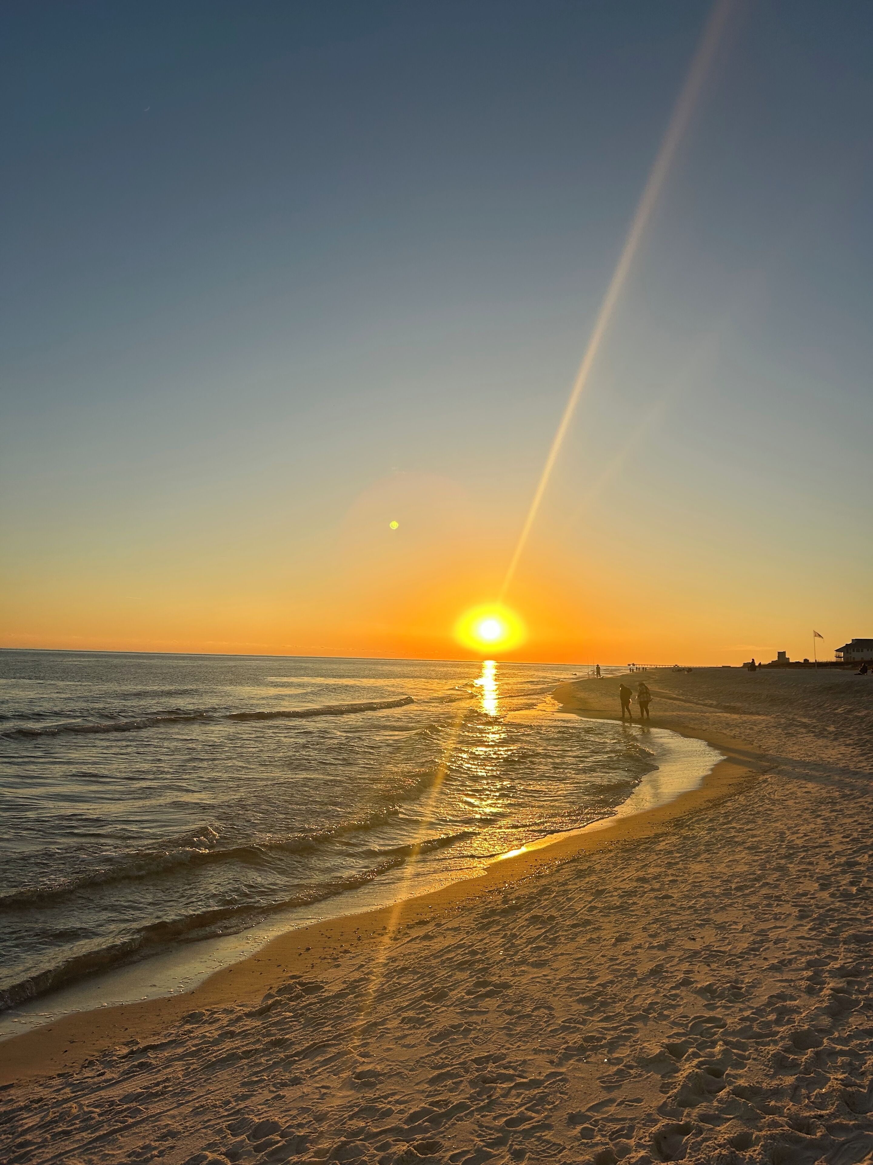 Cena de praia com o sol se pondo sobre o oceano, refletindo na água.