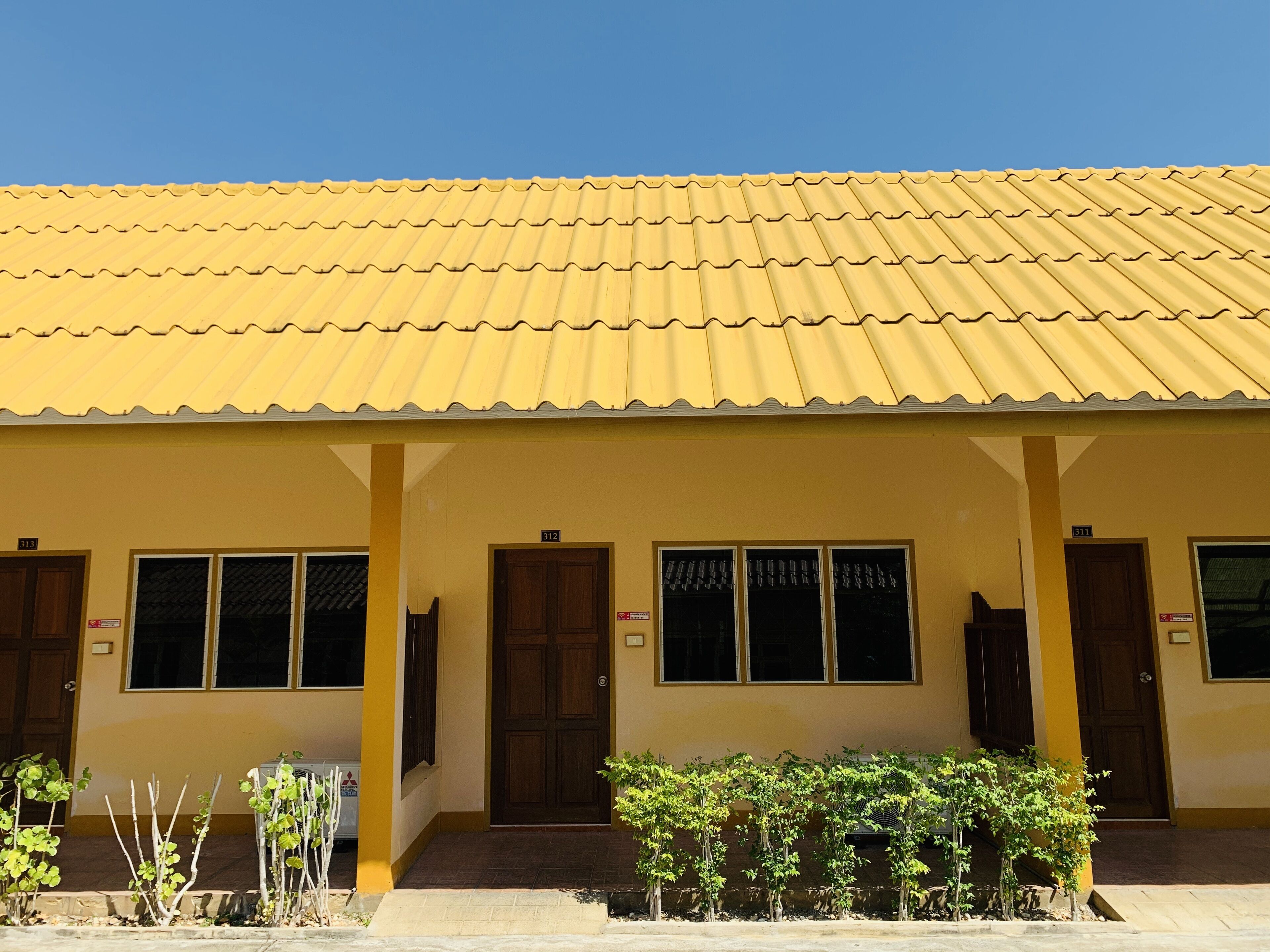 A yellow building with a tiled roof, numbered doors, and windows.