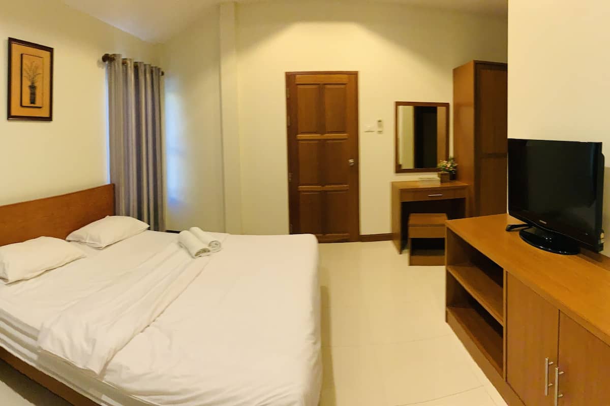Ein Hotelzimmer mit einem Bett, einem Nachttisch aus Holz, einem Fernseher auf einem Holzschrank und einer Tür.