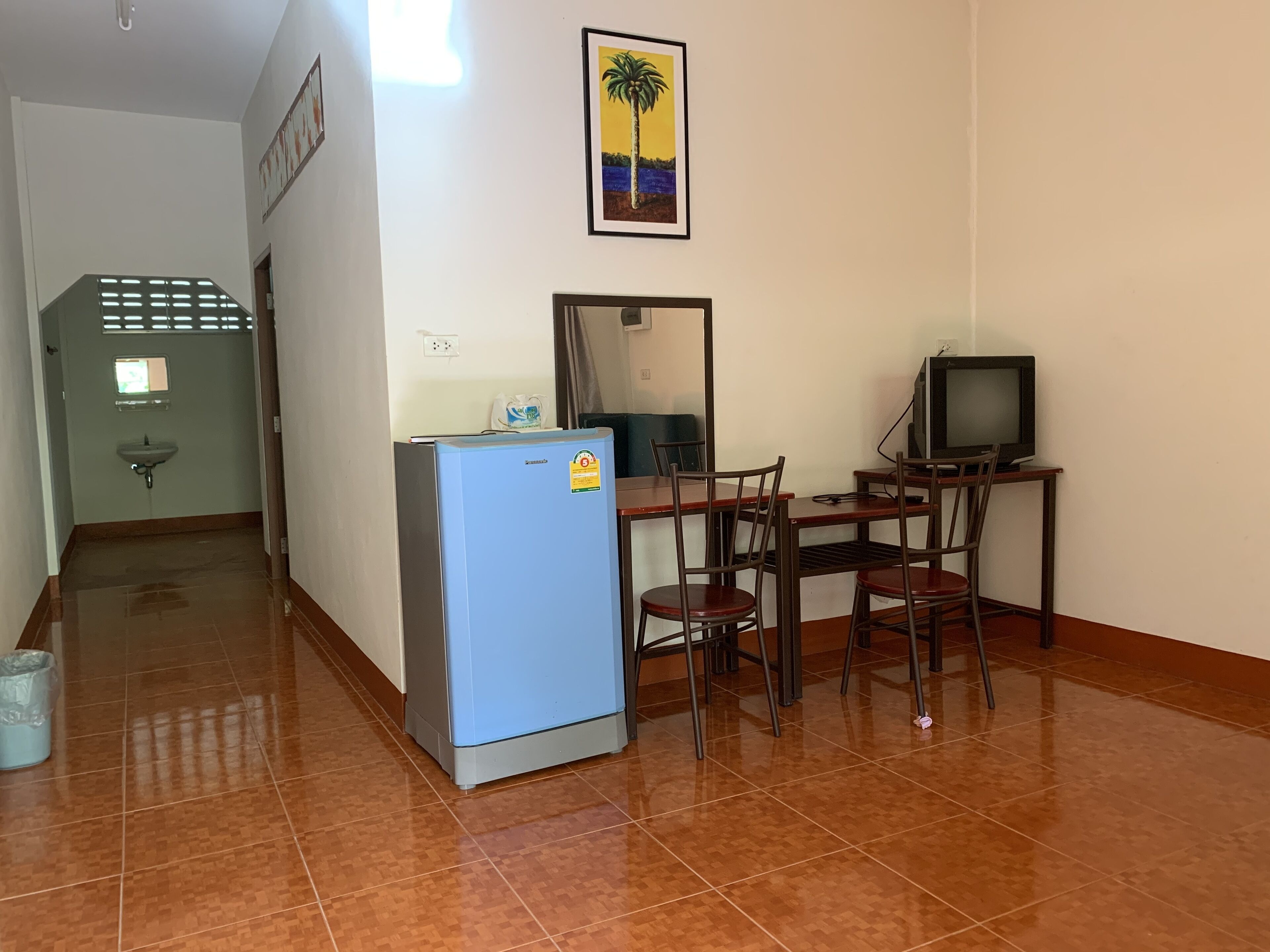 Une pièce de taille modeste comprenant un coin cuisine, une petite table avec des chaises, un téléviseur et un tableau encadré au mur.