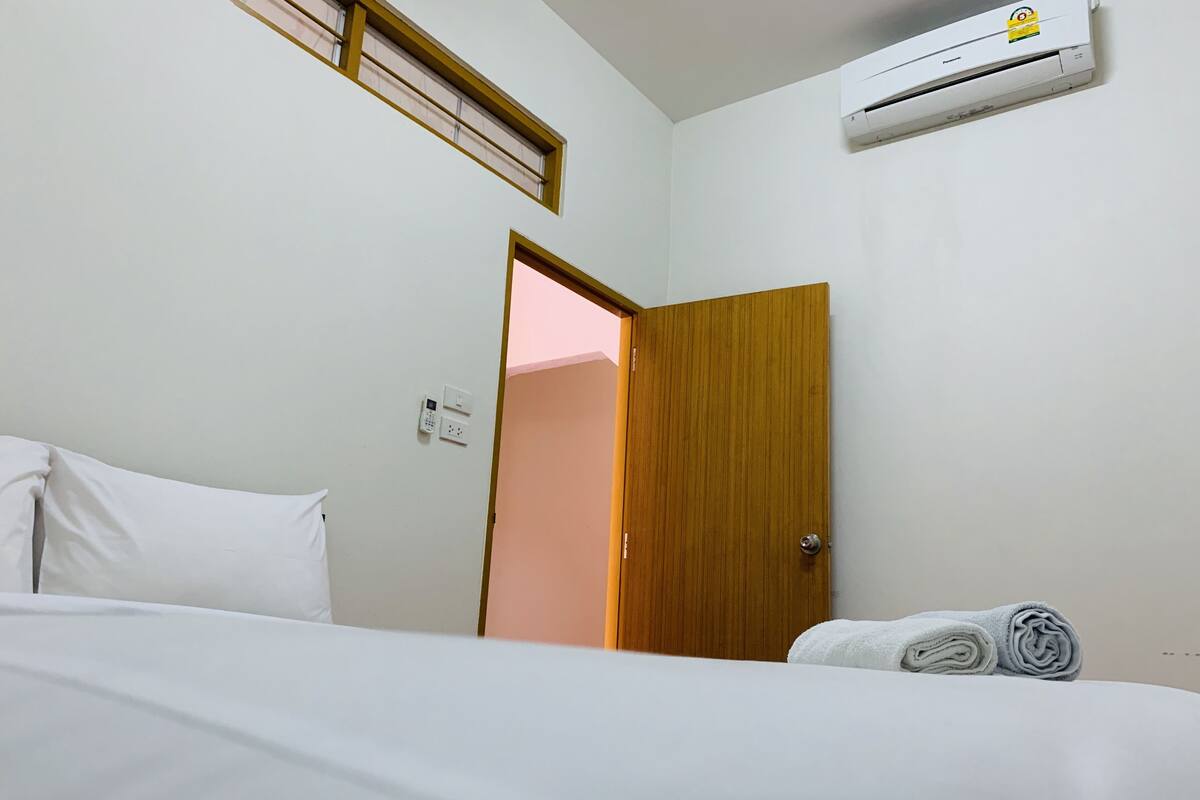 Ein Hotelzimmer mit Bett, einer Holztür, einer Klimaanlage und einem Fenster mit Jalousien.