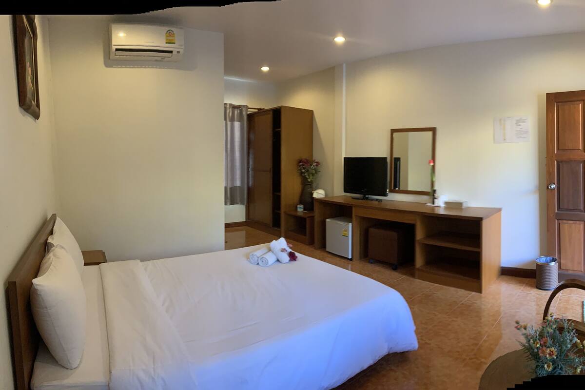 Ein Hotelzimmer mit einem Bett, einem Schreibtisch mit Computer, einem Fernseher und einem Fenster mit Vorhängen.