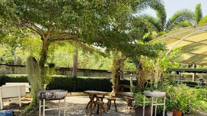 An outdoor seating area with tables and chairs, surrounded by trees and potted plants. - Srisupawadee Resort (Prachuap Khiri Khan)