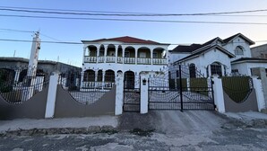 A large white house with a red roof, multiple balconies, and a gated entrance. - Relax and enjoy in this beautiful home in a quiet neighbourhood. (Mineral Hieghts)