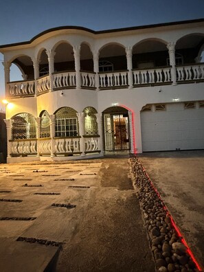 Un edificio de dos pisos con balcón, ventanas en arco y entrada protegida por una reja.