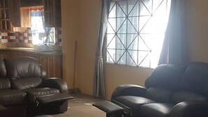 A living room with two black leather sofas, a small table, and a window with a grid pattern. - Relax and enjoy in this beautiful home in a quiet neighbourhood. (Mineral Hieghts)